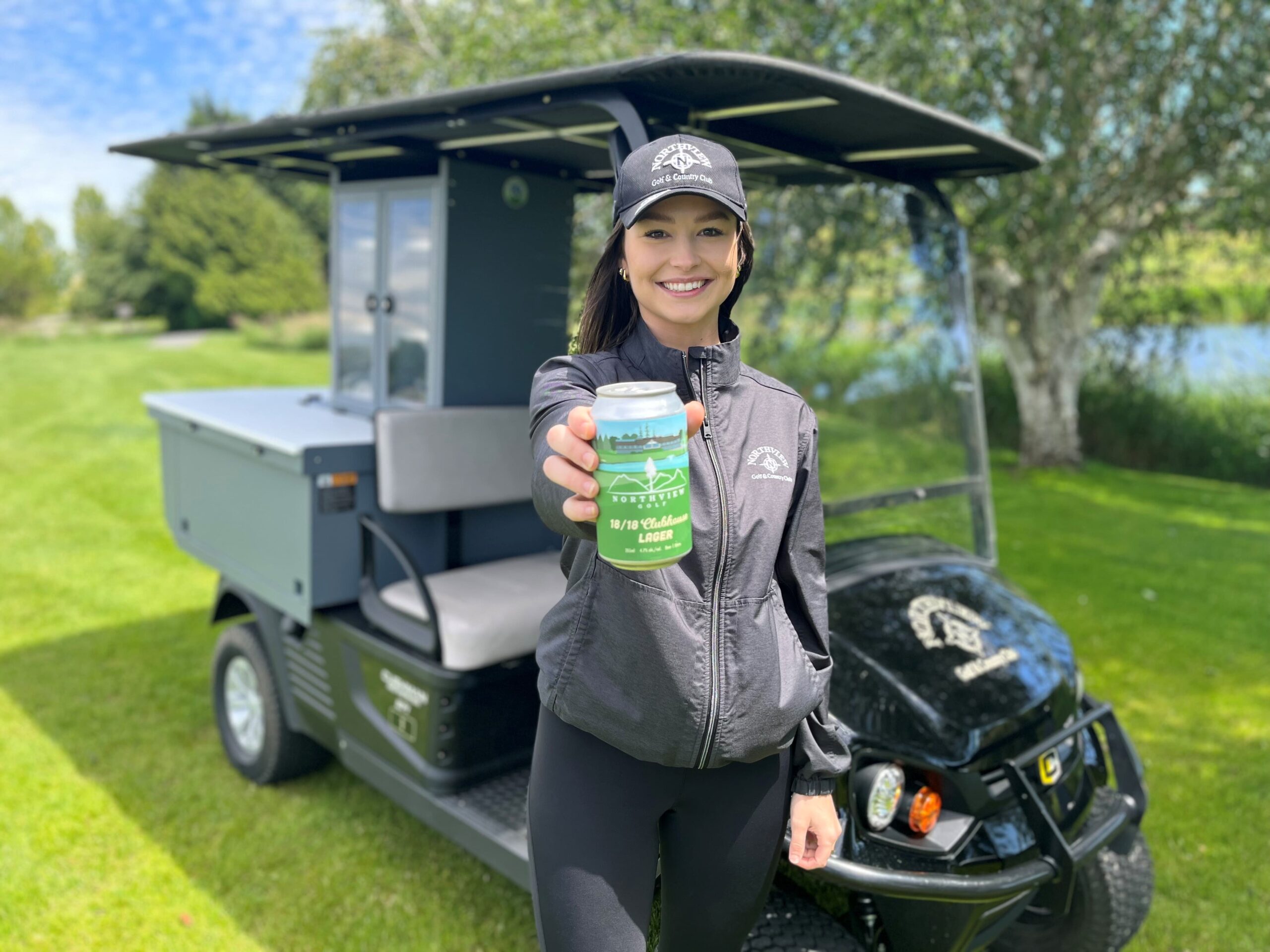 Female golfer wearing Northview Golf apparel smiling at the camera while holding a can of Northview Clubhouse Lager