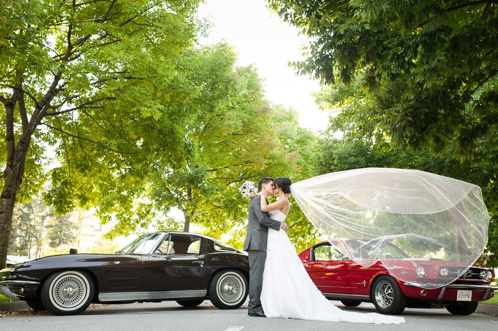 Bride and groom sharing a kiss with two vintage cars behind them