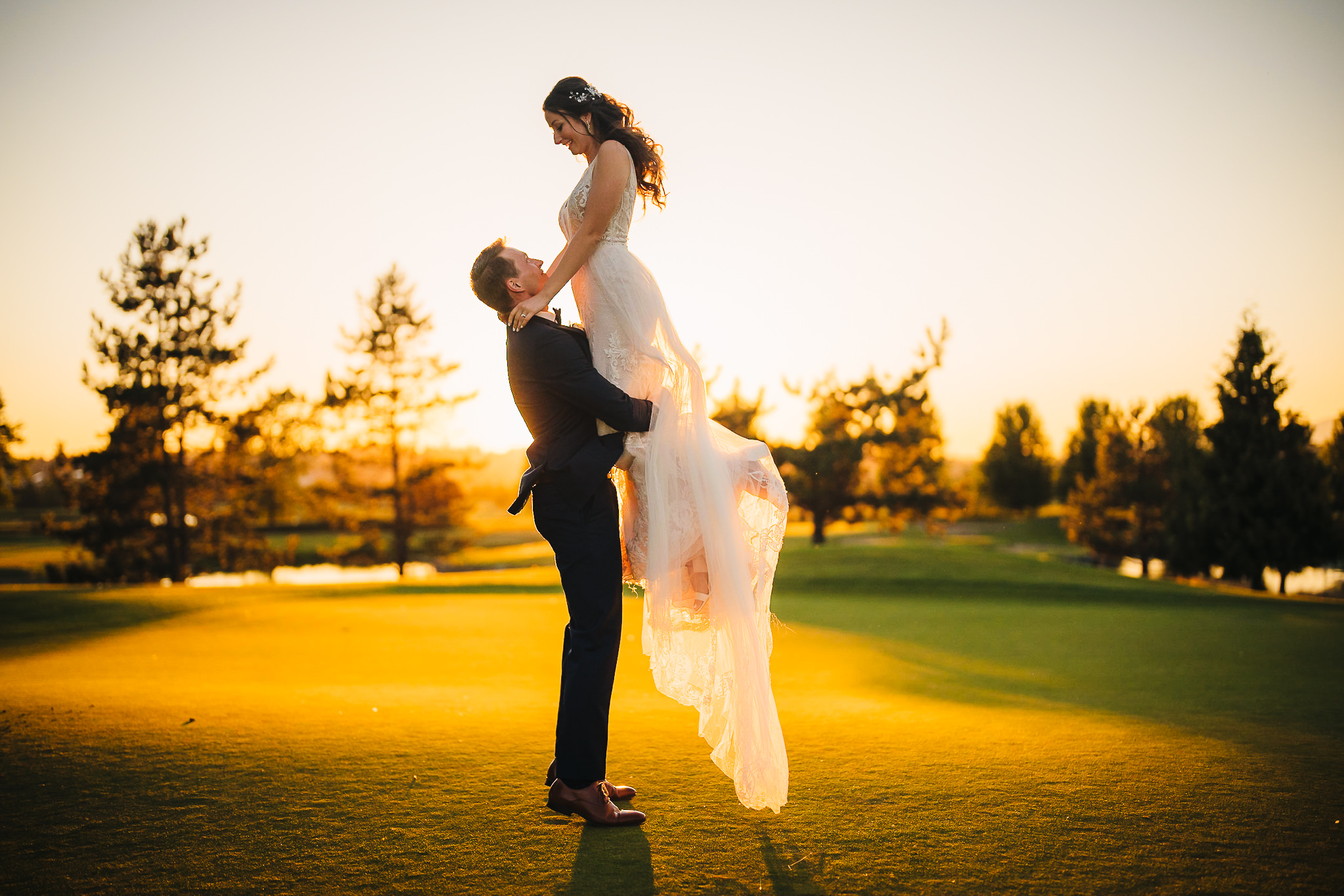 Groom lifting bride while surrounded by lush trees