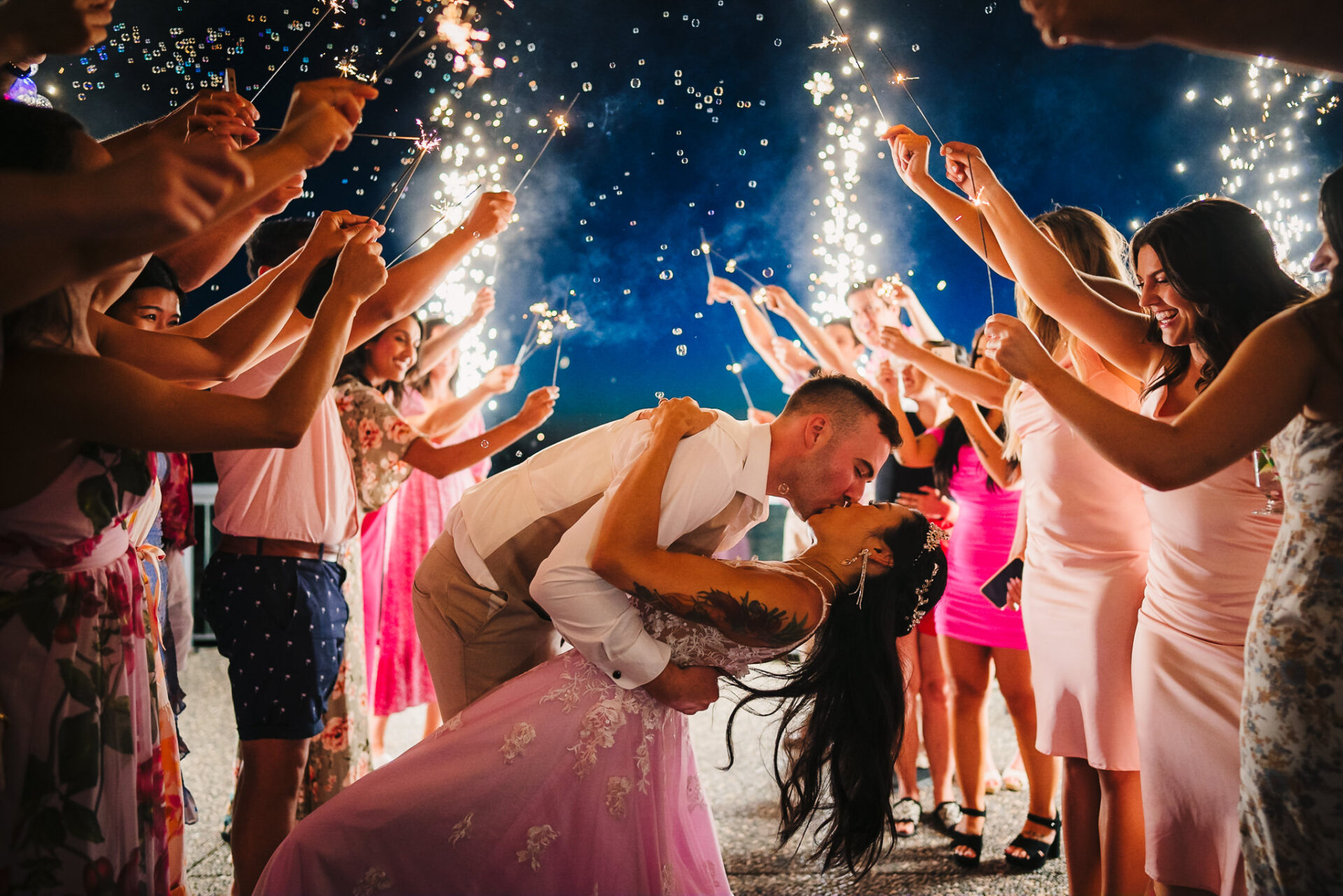 Bride and groom sharing a kiss with guests holding sparklers