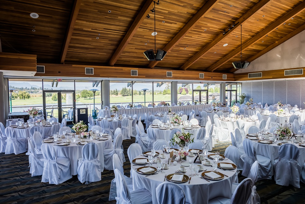 View of tables and chairs set up and decorated in white within the banquet hall