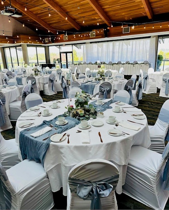View of tables and chairs set up and decorated in white within the banquet hall
