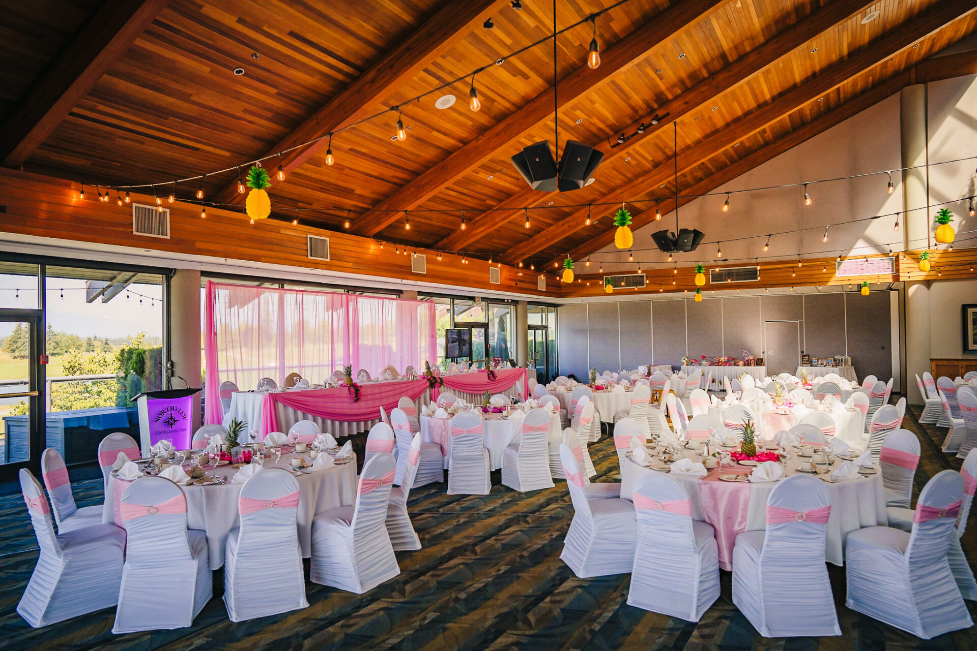 View of tables and chairs set up and decorated in both white and pink within the banquet hall