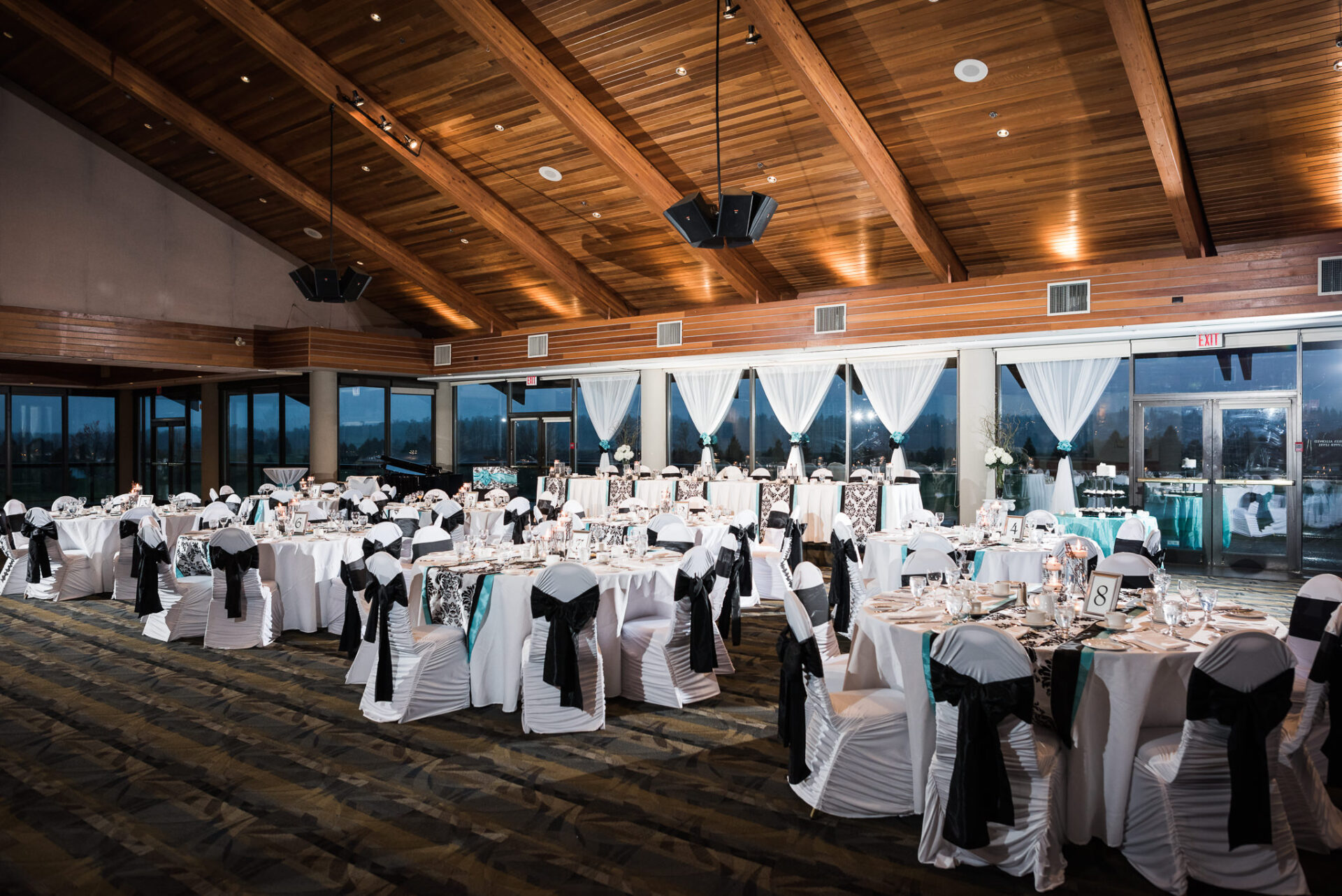 View of tables and chairs set up and decorated in both white and black within the banquet hall