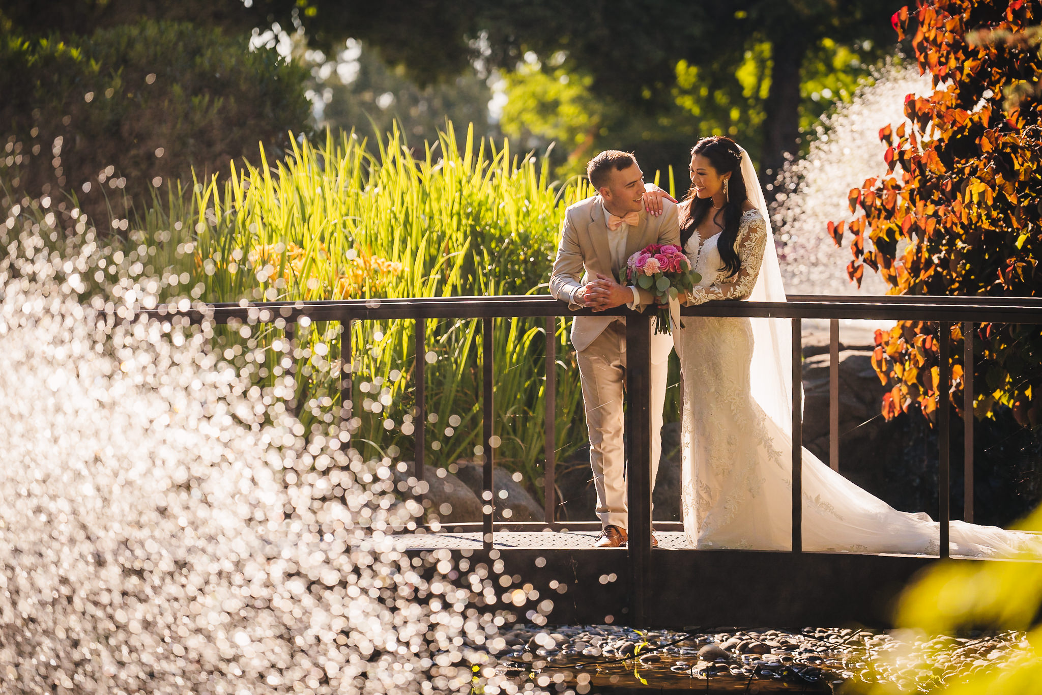 Bride and groom smiling at each other on the bridge within the enchanted garden