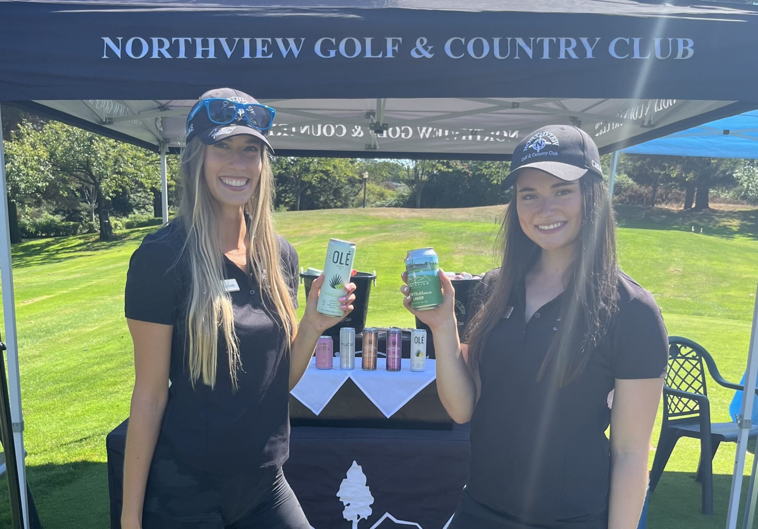 Two female volunteers smiling at the camera while holding canned beverages
