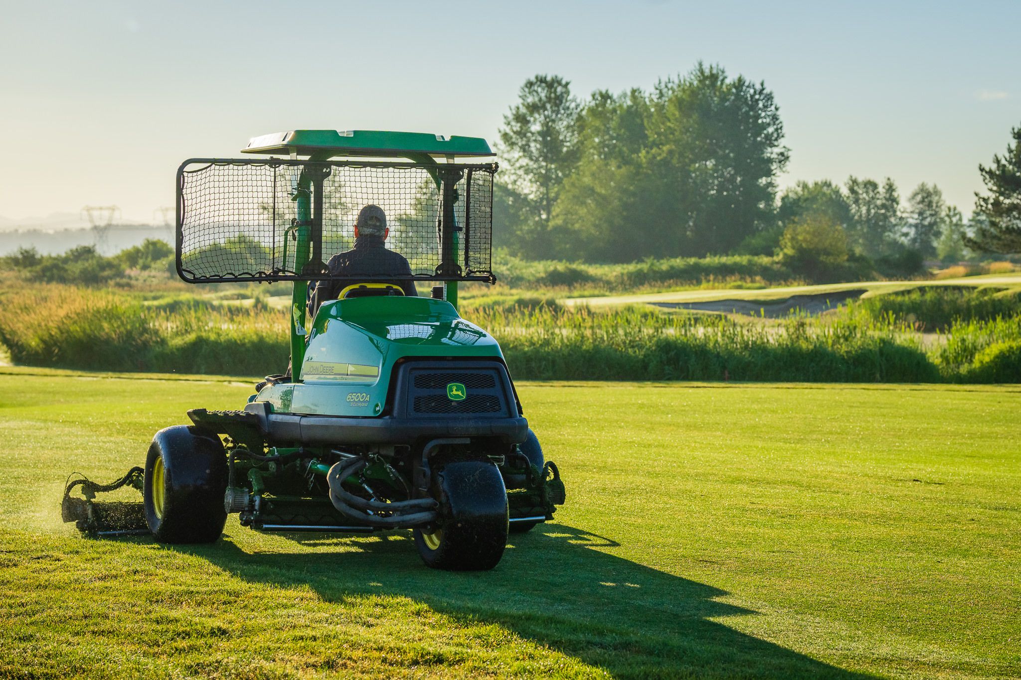 Operator driving a grass cutting vehicle on the golf course